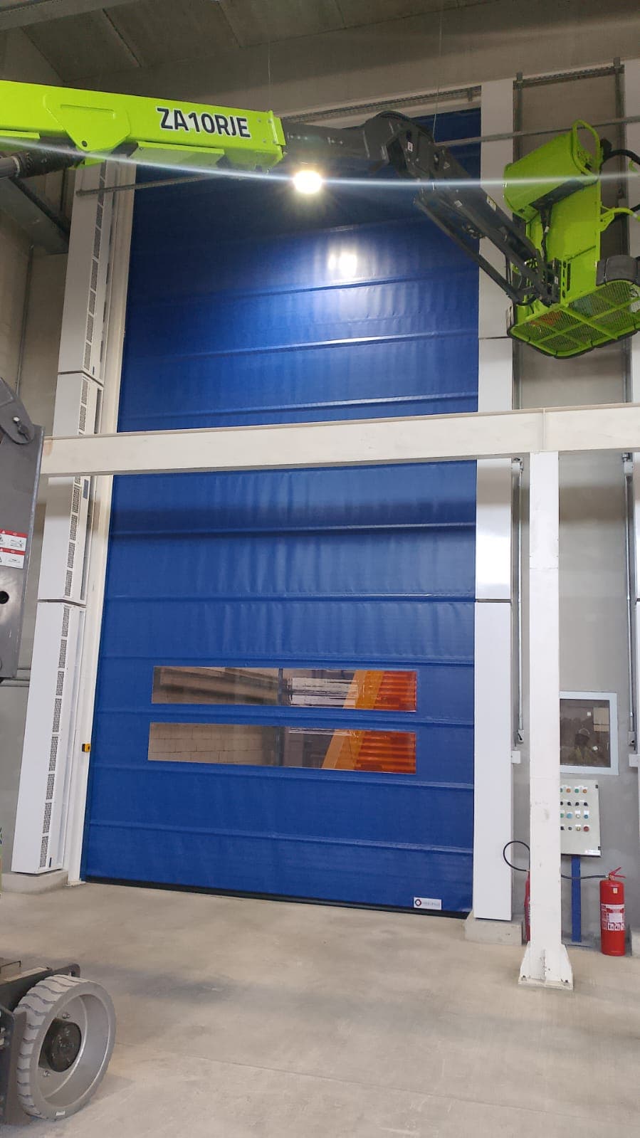 Cortinas de ar verticais nas laterais de porta azul fechada, com plataforma elevatória no local